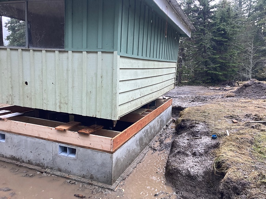The small building on temporary cribbing above a newly poured foundation wall
