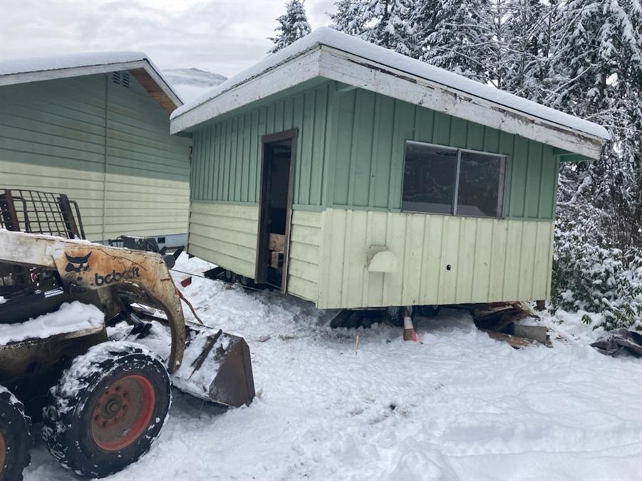 The small building on its moving dolly, a skid-steer alongside for scale, in the snow
