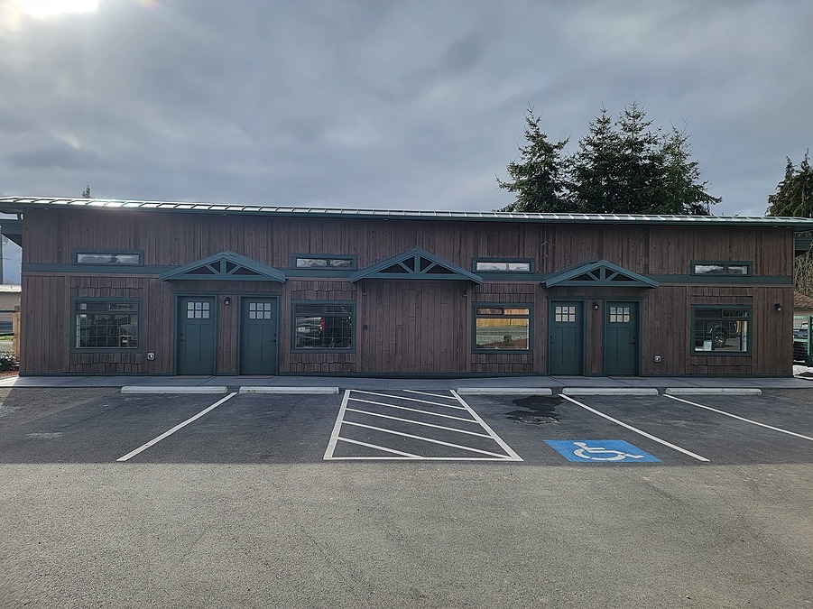 The renovated Dungeness Valley Inn, with board-and-batten siding, four guest suite entries and a paved striped parking area