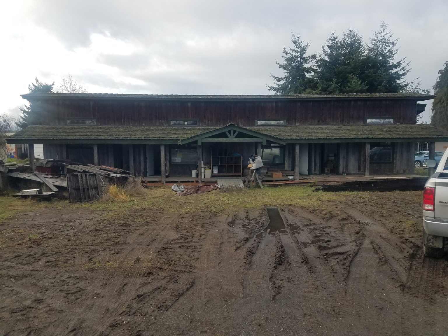 Derelict roadside building before renovation, with sagging moss-covered roof and a churned mud lot