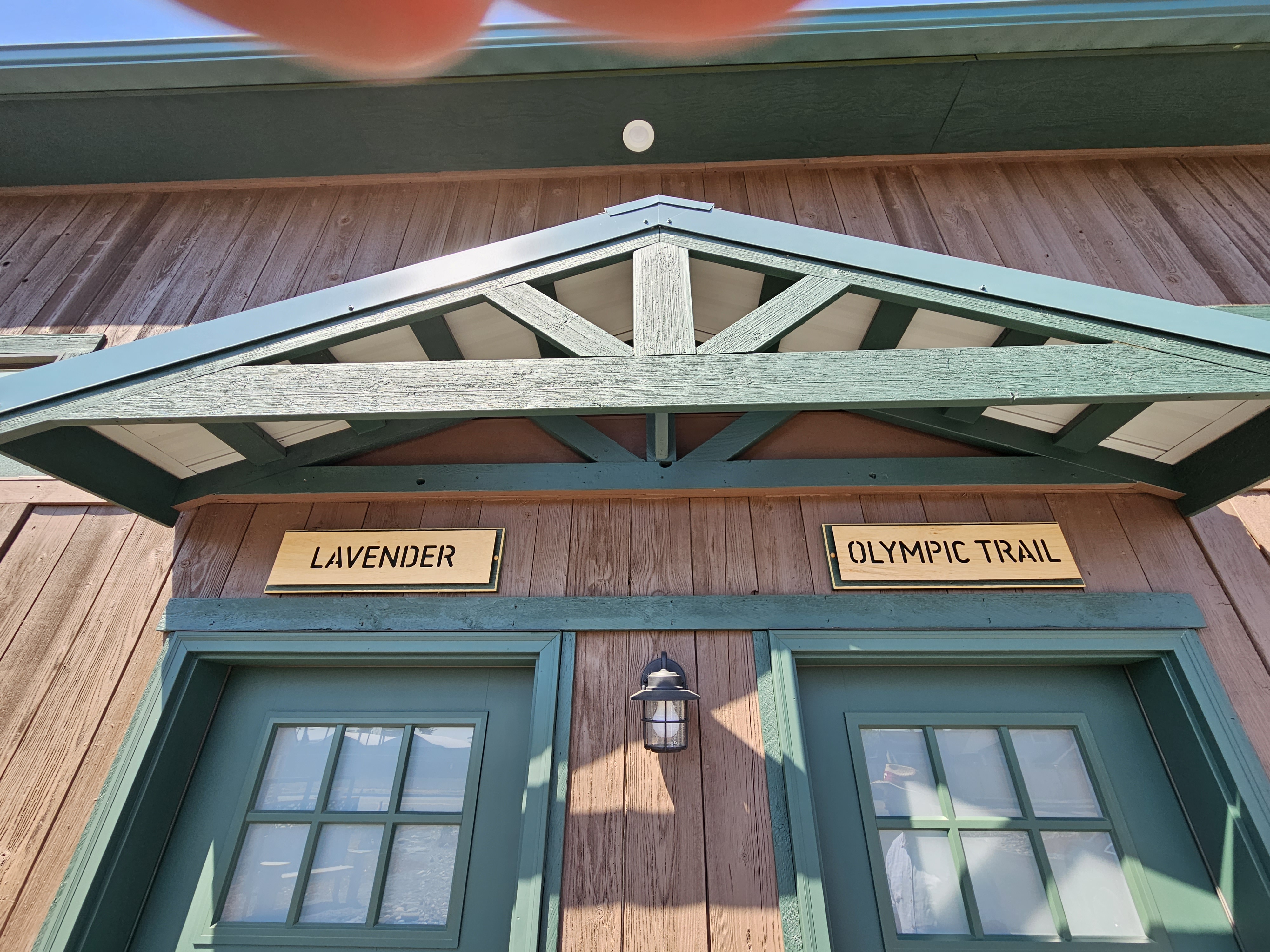 Two guest suite entries under a green timber gable, with hand-lettered signs reading Lavender and Olympic Trail