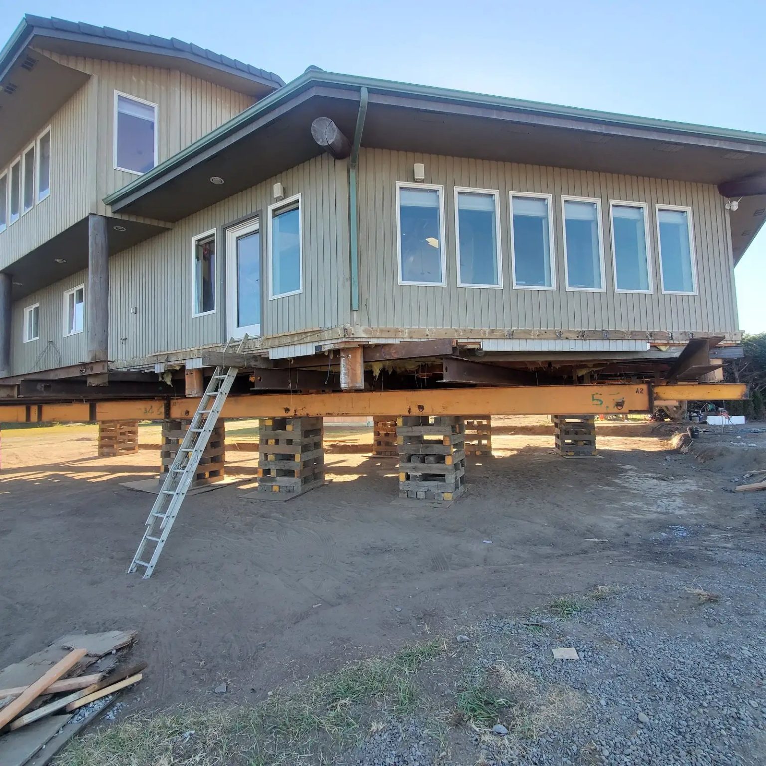 A relocated house raised on timber cribbing, with a ladder reaching up to the door showing how far off the ground it stands.