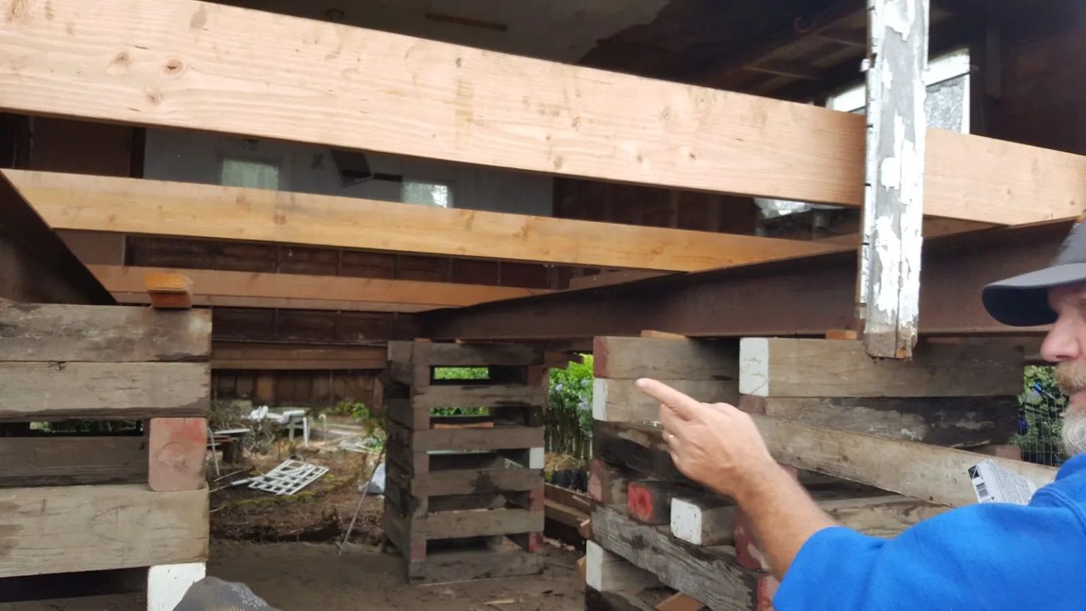 The 1920s garage lifted clear of the ground on timber cribbing and steel beams, with daylight visible beneath the structure