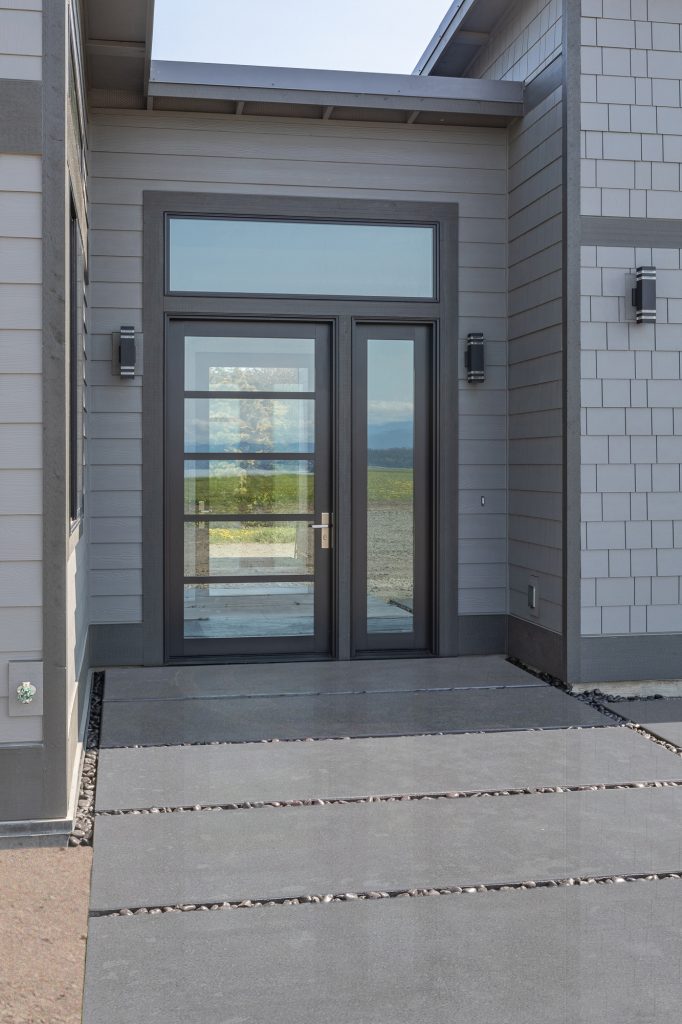 Covered entry with glazed double doors framing a view straight through the house to the landscape beyond
