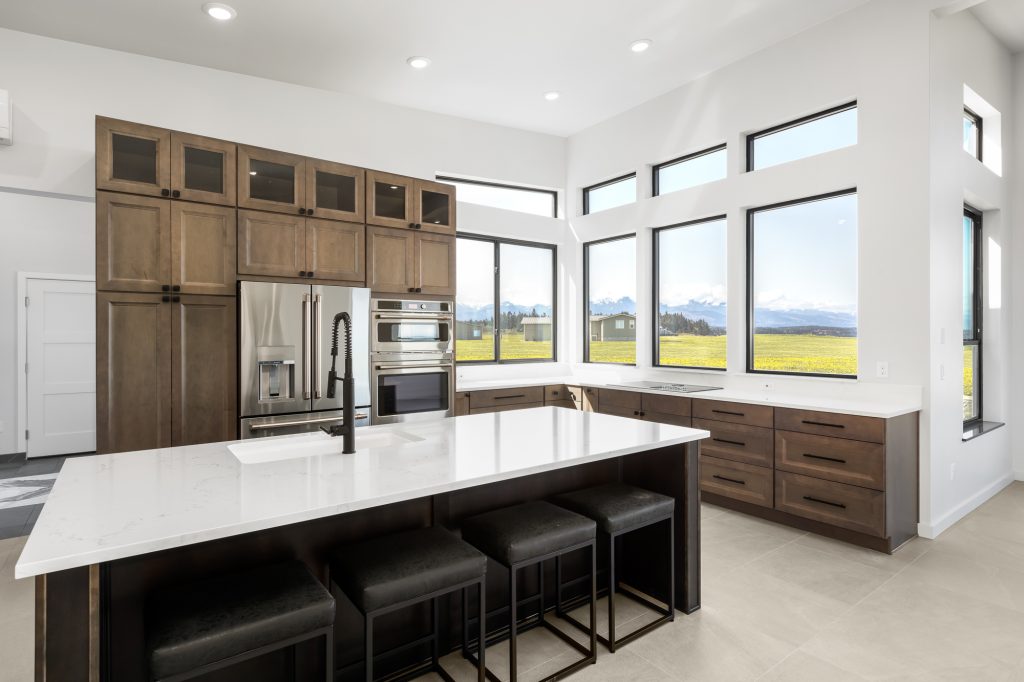 Custom kitchen with walnut cabinetry, quartz waterfall island and corner windows framing the Olympic Mountains