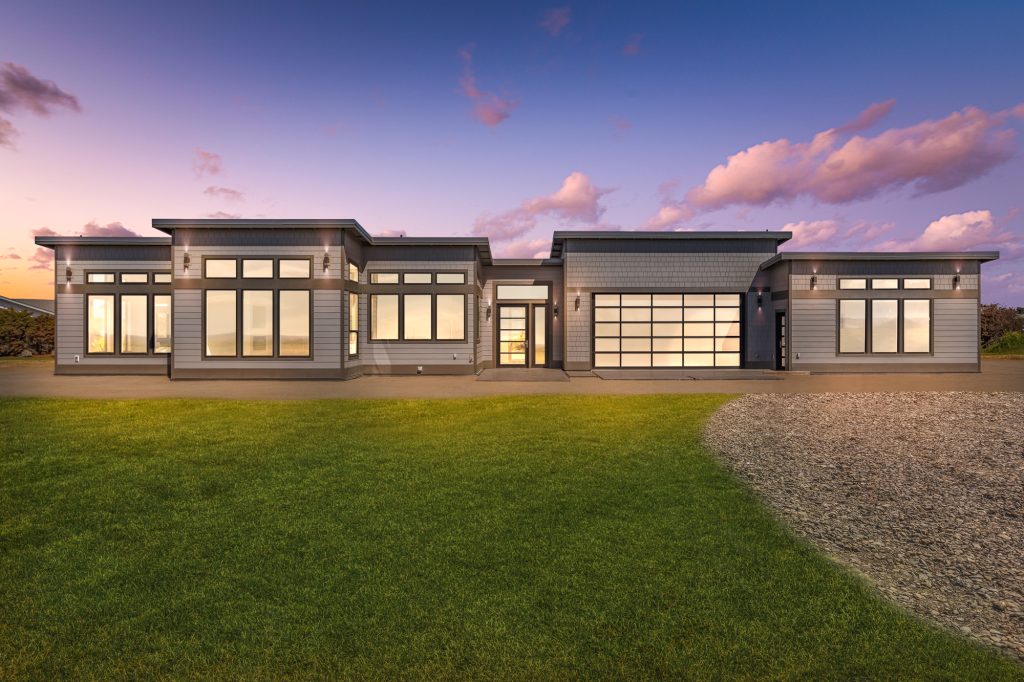 Modern single-storey custom home near Sequim at twilight, warm interior light glowing through full-height windows